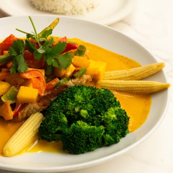 Thai curry with chicken, mango, bell peppers, broccoli, baby corn, and cilantro on a white plate.