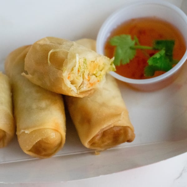Golden-fried Thai spring rolls with a sweet chili dipping sauce, one roll cut open to show filling.