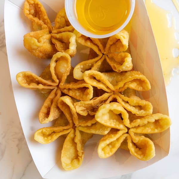 Crispy golden fried wontons, shaped like flowers, with a side of sweet chili sauce in a white container.
