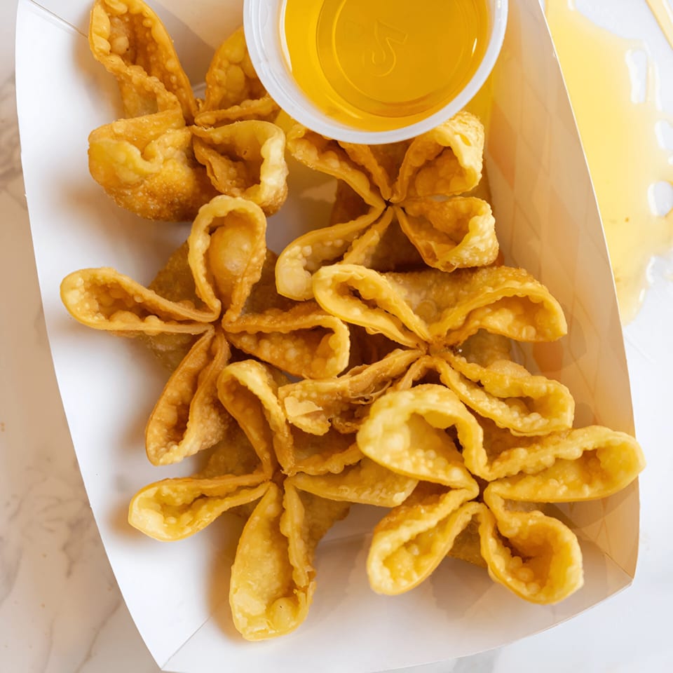 Crispy golden wontons arranged in a white paper tray with a side of dipping sauce.