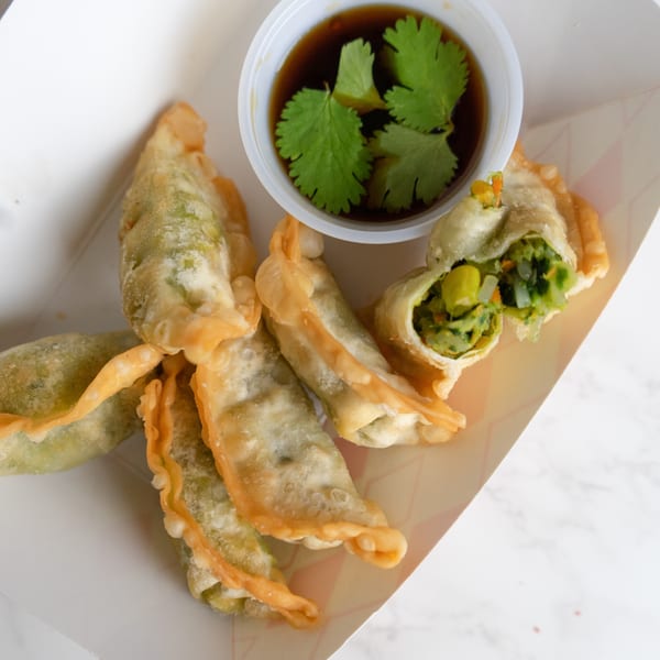 Crispy Thai vegetable dumplings with a side of soy sauce and cilantro in a white container.