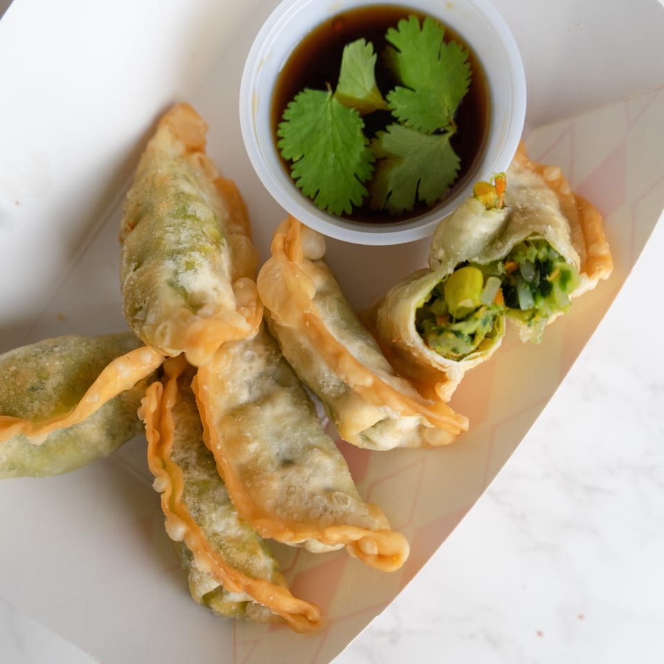 Crispy Thai vegetable dumplings with a side of soy sauce and cilantro in a white container.