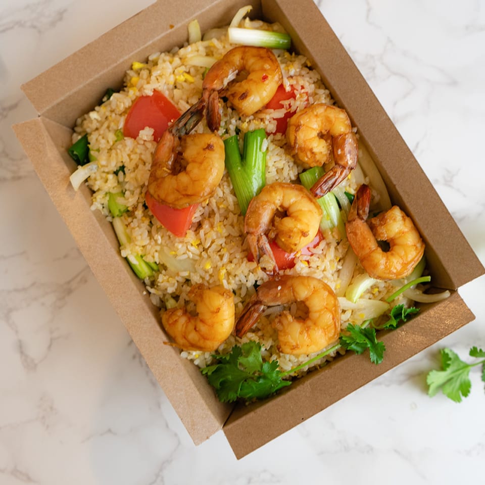Thai shrimp fried rice with red peppers, green onions, and cilantro in a takeout box.
