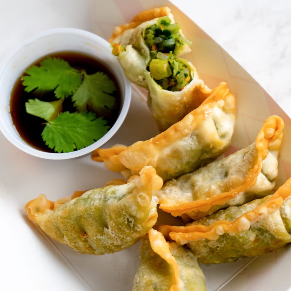 Crispy fried Thai dumplings with green filling and a side of soy sauce with cilantro.
