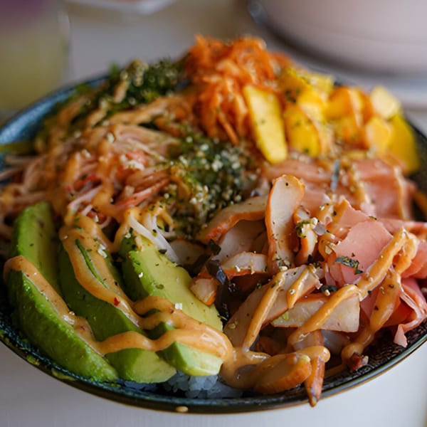 Close-up of a vibrant Thai dish with avocado, mango, crab, and various toppings in a bowl.