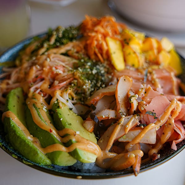 Close-up of a colorful Thai poke bowl with avocado, mango, crab, and various toppings.