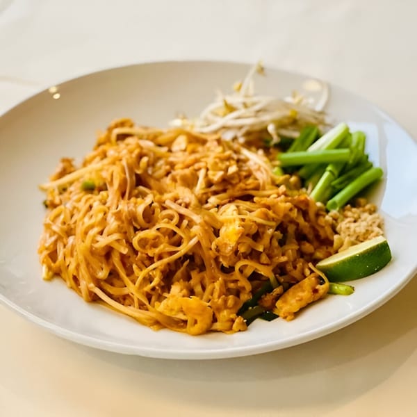 A plate of Cilantro Thai Express Pad Thai with noodles, bean sprouts, green onions, and lime.