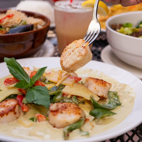 Fork lifting a scallop from a plate of Thai green curry with scallops and vegetables.